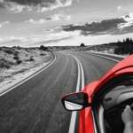 Red car driving on a road under an open sky